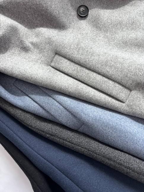 Wool coats stacked in grey, blue and navy showing the pocket detail