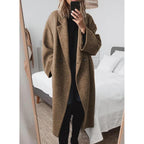 Brown long wool coat worn over an all-black outfit in a bright bedroom